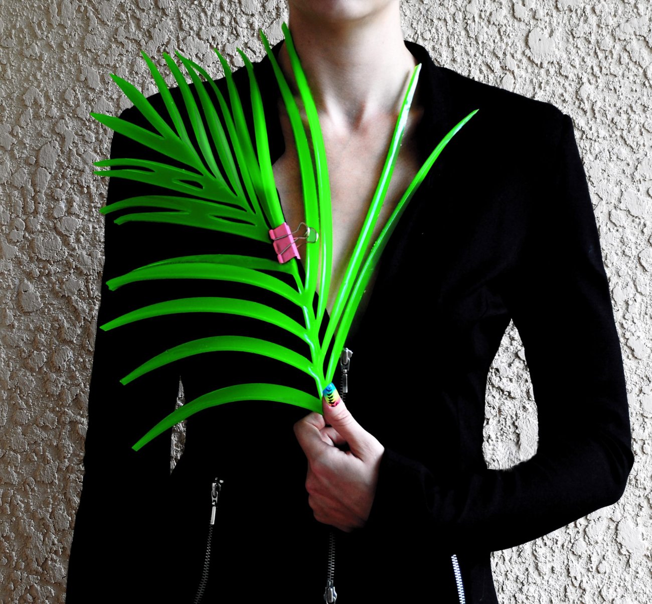 Photograph of figure wearing black jacket holding a palm leaf with a pink binder clip attached.